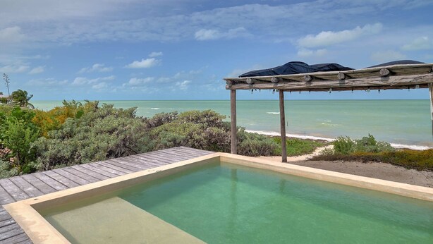 An infinity pool with a wooden deck and a pergola with umbrellas overlooking the ocean. - Casa Almeja - Yucatan Home Rentals (Chicxulub)