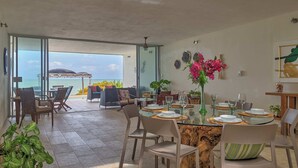 An open-plan dining area with a view of the sea, furnished with chairs and tables, and decorated with a vase of flowers. - Casa Almeja - Yucatan Home Rentals (Chicxulub)