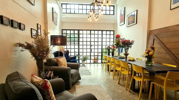 A modern living room with a sofa, a dining table with yellow chairs, and a large window with a view.