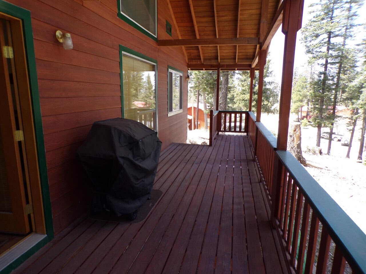 A wooden deck with a covered grill, a railing, and a view of trees.
