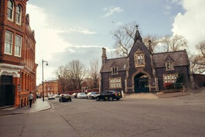 A historic building with a prominent entrance and large windows, situated on a street with parked cars and a sidewalk.