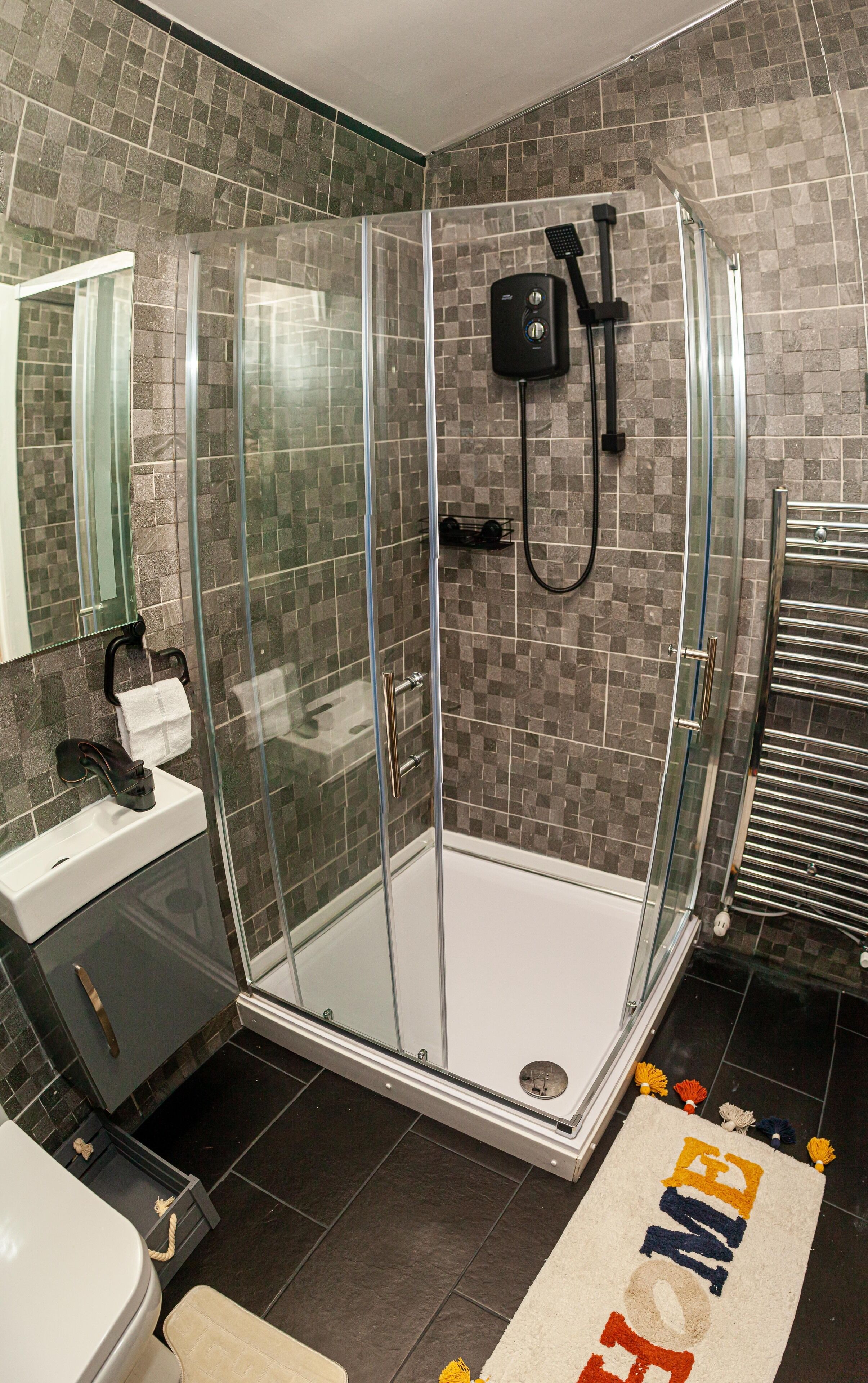 A modern bathroom with a glass-enclosed shower, a sink with a towel rack, and a toilet.