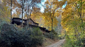 A rustic cabin with a porch, surrounded by autumn foliage and a dirt path.