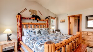 A wooden bed with a bear headboard, a bedside table with a lamp, and a wooden bench.