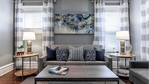 Ett modernt vardagsrum med en grå soffa, två sidobord med lampor, ett soffbord och en stor, abstrakt tavla på väggen.