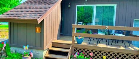 A small wooden cabin with a porch, a mailbox, and a garden with flowers and American flags.