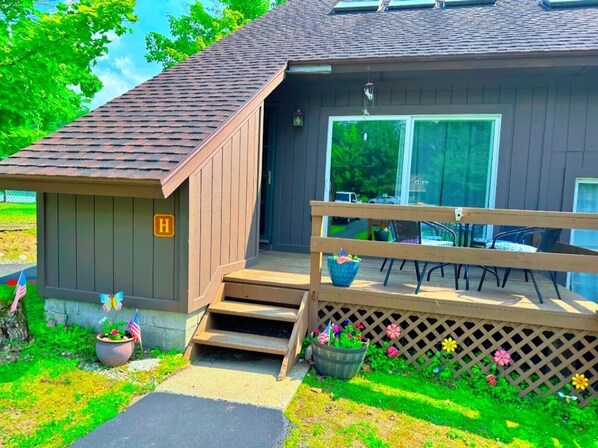A small wooden cabin with a porch, a mailbox, and a garden with flowers and American flags.