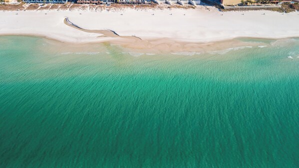 An aerial view of a beach with clear turquoise waters and a sandy shoreline.