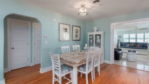 A dining area with a wooden table and white chairs, a white cabinet, and framed artwork on the wall.
