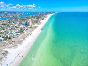 A coastal cityscape with a long sandy beach, clear blue waters, and a dense urban area with high-rise buildings.
