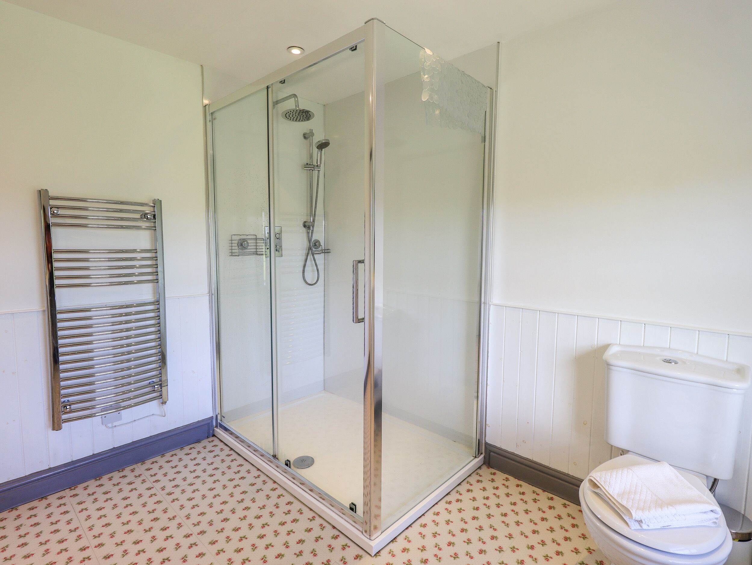 A modern bathroom with a glass-enclosed shower, a white toilet, and a patterned floor.