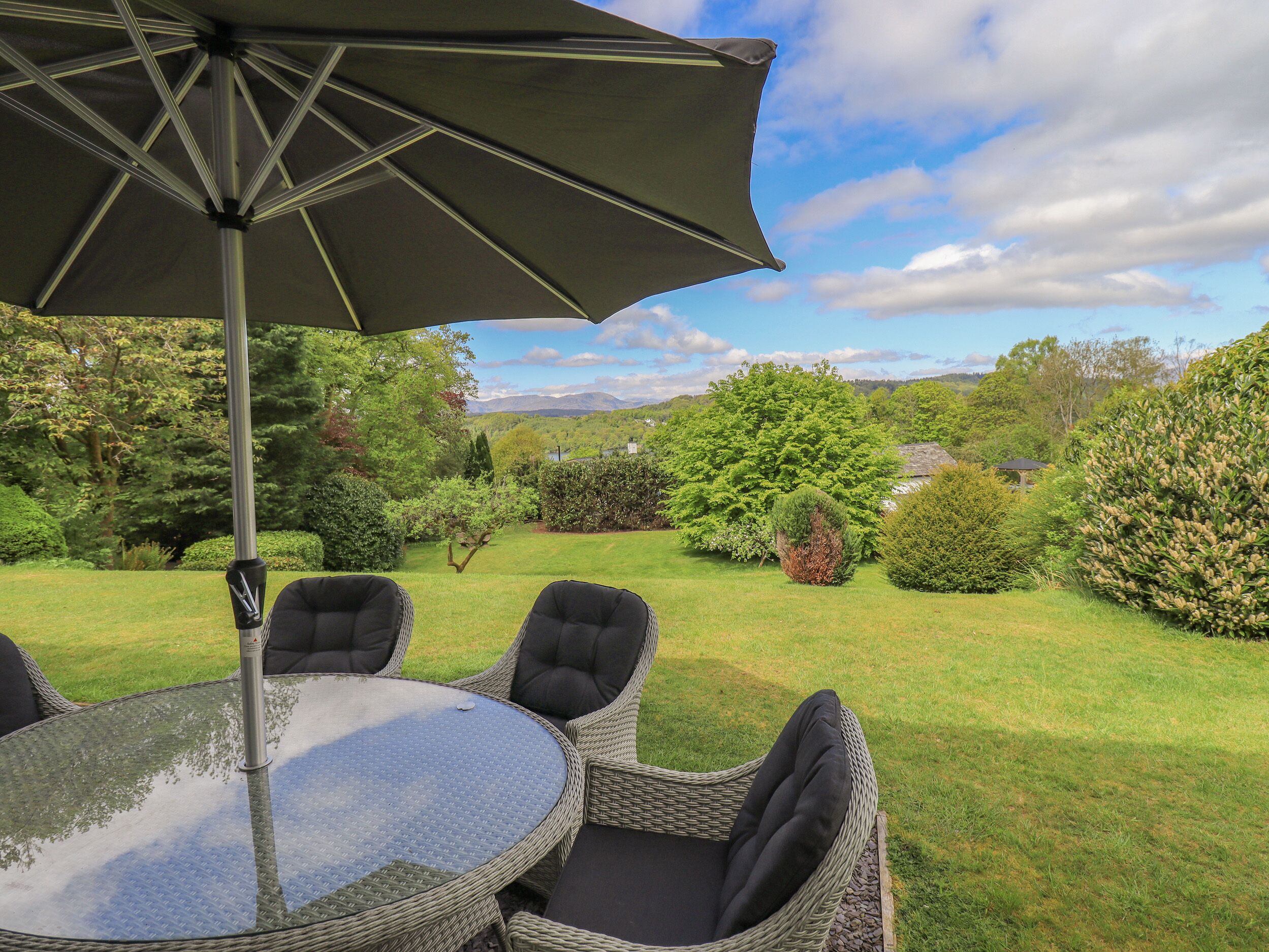 A patio with wicker furniture, a glass table, and a large umbrella.
