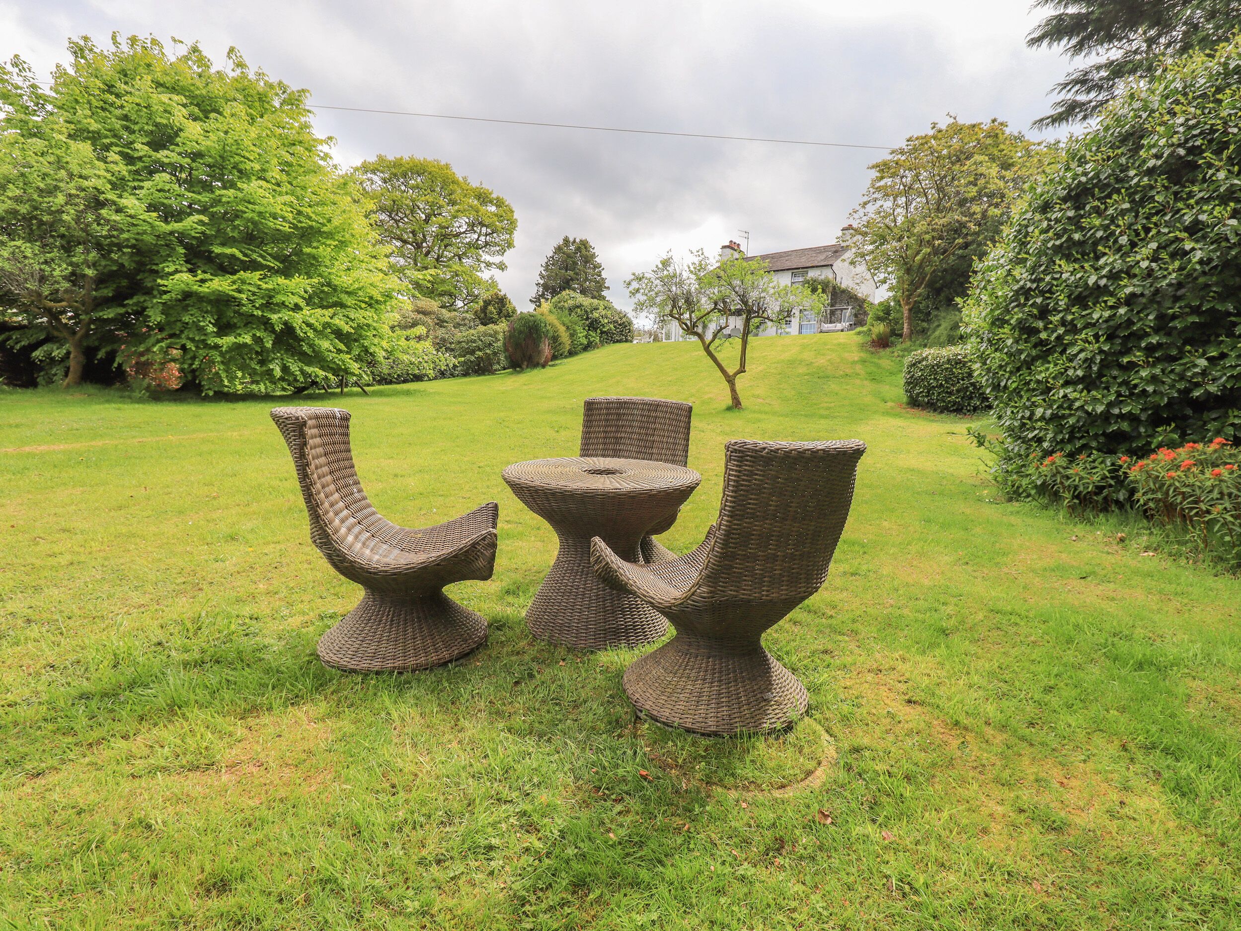 Wicker furniture in a grassy outdoor area with trees and a building in the background.