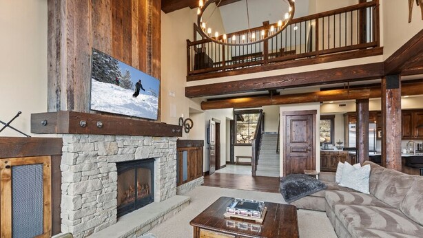 A spacious living area with a stone fireplace, a large television mounted on the wall, a wooden staircase, and a cozy seating area.