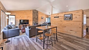 Un salon moderne avec un intérieur en bois, un téléviseur à écran plat, un canapé, une table basse et un coin repas avec des tabourets.