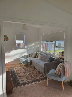 Un salon chaleureux avec un canapé d’angle, un tapis à motifs et une vue sur une cour clôturée, visible à travers de grandes fenêtres.