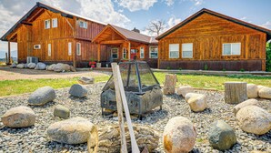 A wooden cabin with a porch, a fire pit, and a shovel.