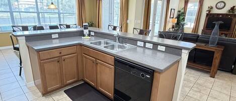 A kitchen with a dishwasher, a sink, and a dining area with chairs.