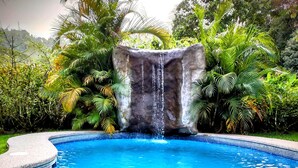 Ein klares, blaues Schwimmbecken mit Wasserfall, umgeben von üppiger Vegetation.