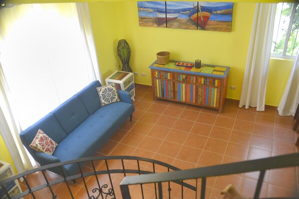 A living room with a blue sofa, a bookshelf, and a painting of boats on the wall. - Paradise Found! Character filled close to beach, forest and amenities (Puntarenas Province)