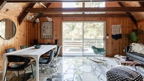 A wooden interior with a dining table, chairs, a sofa, and a large window. - Come enjoy nature in our cabin !  (Idyllwild-Pine Cove)
