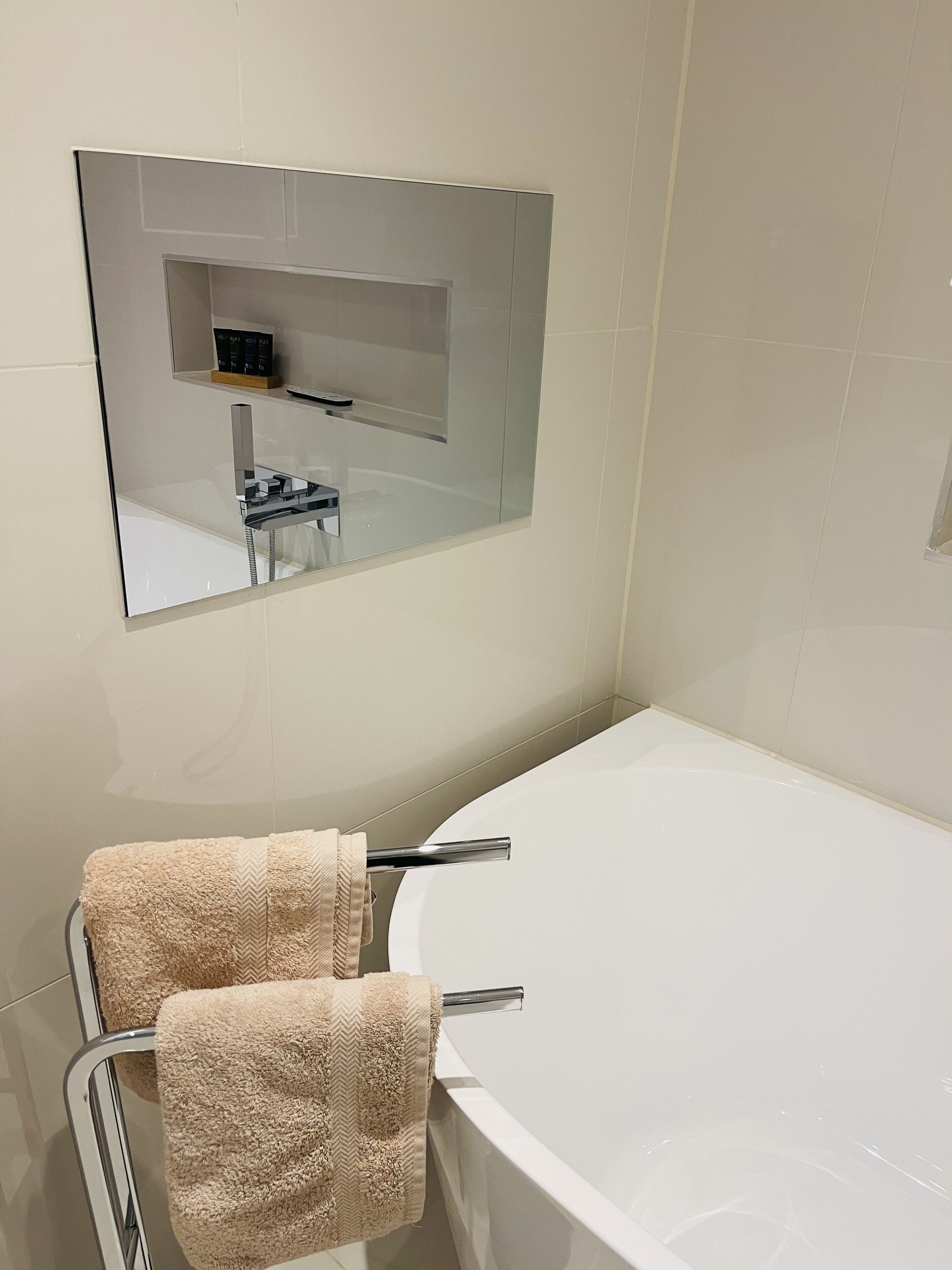 Ein Badezimmer mit einem großen Spiegel, einer Badewanne und zwei Handtüchern, die an einem Handtuchhalter hängen.