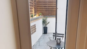 A view through a door into a patio area with a table and chairs, a potted plant, and a wooden fence. - Escape London in London - 2 bed luxury apartment in lovely Wanstead (London)