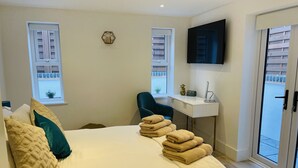 A bedroom with a bed, two windows, a desk, a chair, a TV, and a door. - Escape London in London - 2 bed luxury apartment in lovely Wanstead (London)
