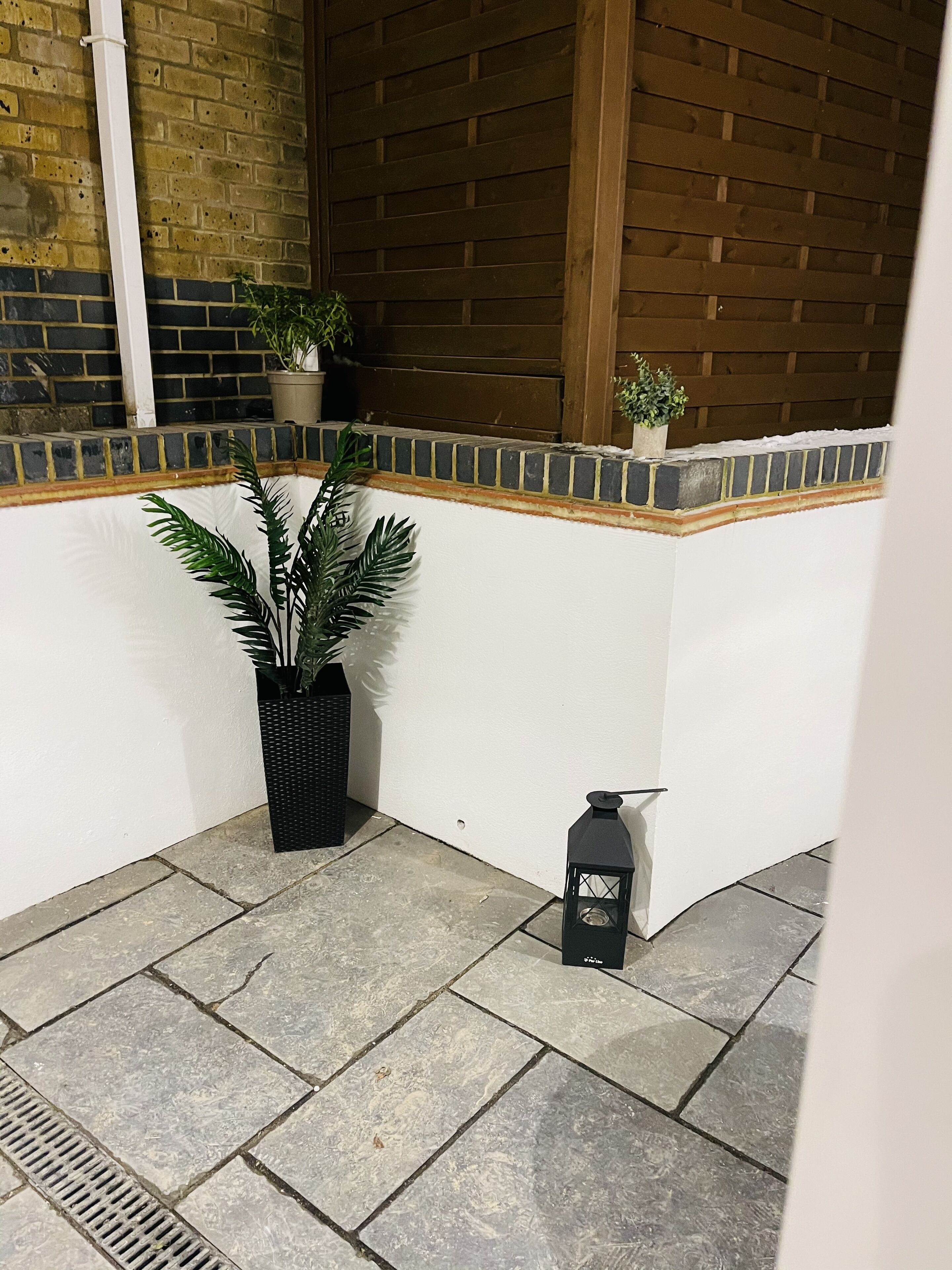 A corner with a potted plant, a lantern, and a tiled floor.