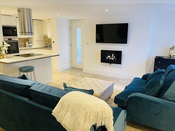 A modern living room with a sofa, ottoman, and a flat-screen TV mounted on the wall.
