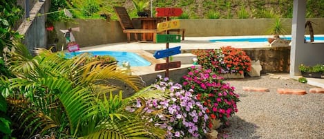 Un área de piscina con un cartel, muebles de exterior y diversas plantas.