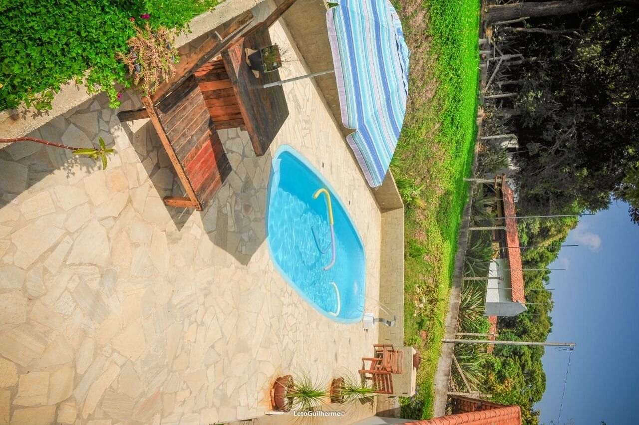 Piscina com deck de madeira e espreguiçadeiras, cercada por vegetação e um terraço de pedra.