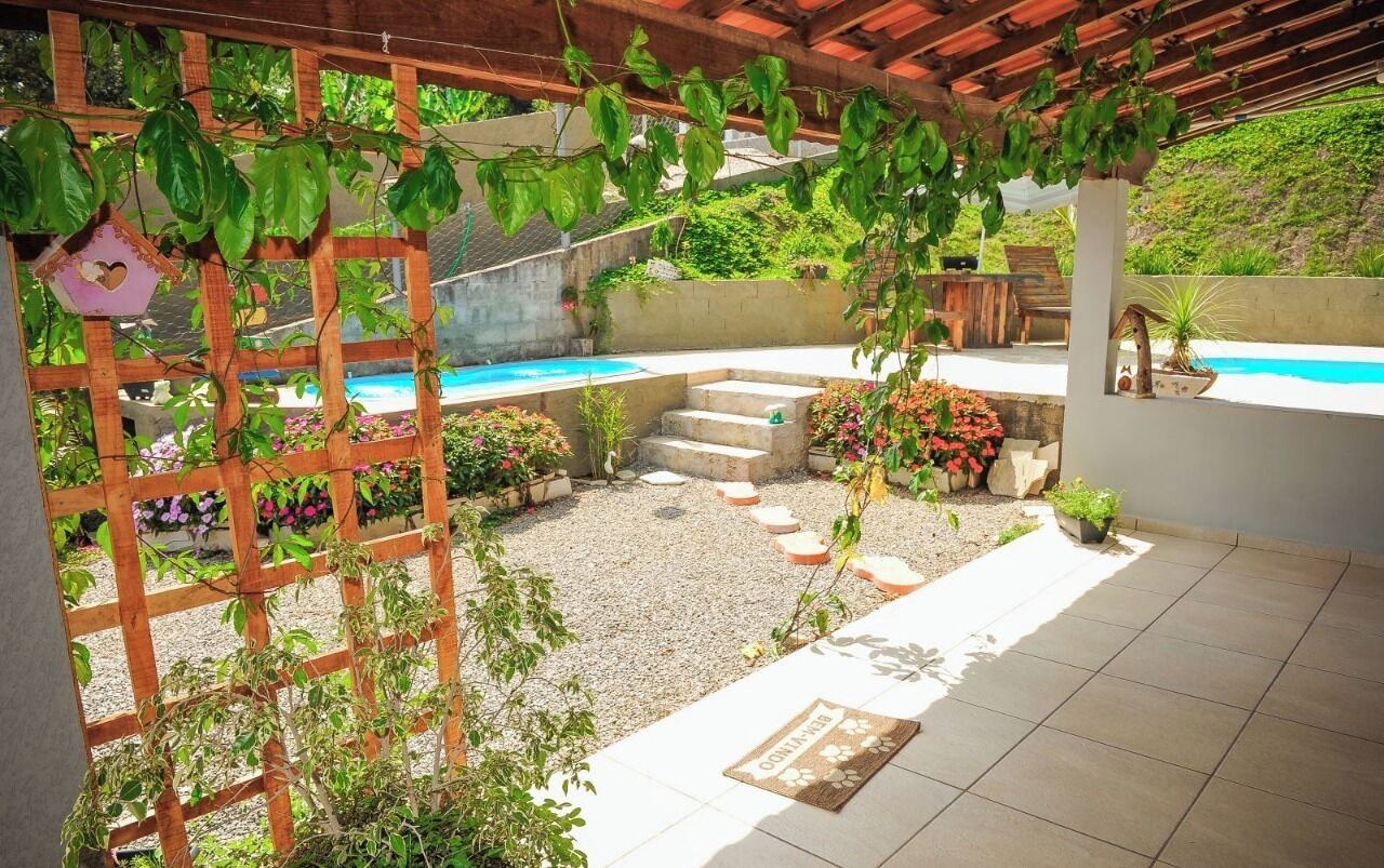 A covered patio area with a pool, surrounded by plants and a wooden trellis.