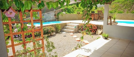 Un área de patio techada con piscina, rodeada de plantas y una pérgola de madera.