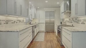 A kitchen with white cabinets, a stainless steel range hood, and a wooden floor. - Midtown Rancher with Great Backyard and Deck for Entertaining (Tulsa)