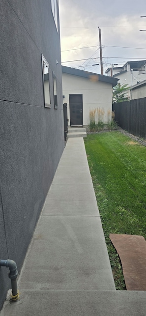 A concrete pathway leading to a modern building with a dark facade and a door.