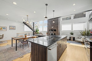 Una cocina moderna con una isla central, un comedor con mesa y sillas de madera, y una escalera que lleva a un nivel superior.