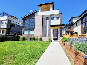 A modern two-story residential building with a central entrance, a covered porch, and a well-maintained lawn.