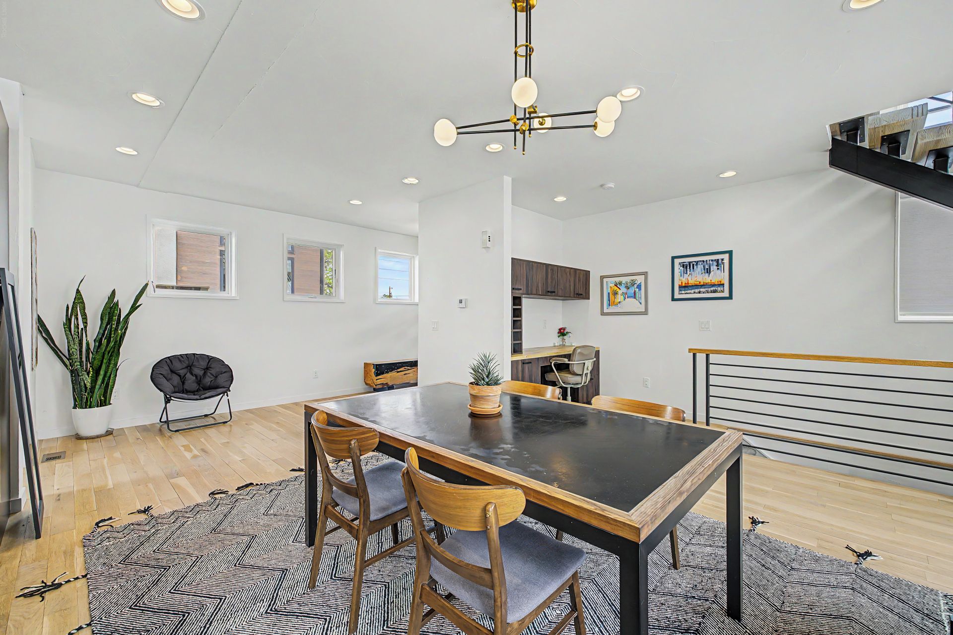 A modern dining area with a black table, wooden chairs, and a hanging light fixture.