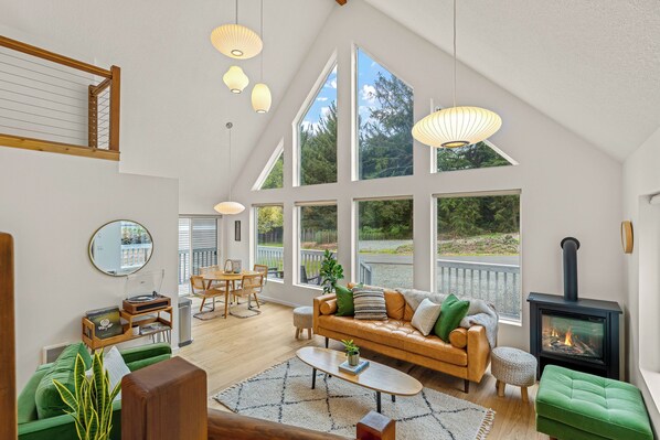 A spacious living area with a high ceiling, large windows, a fireplace, and a cozy seating arrangement.