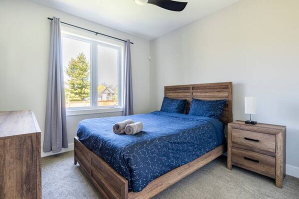 A bedroom with a wooden bed, a nightstand, a window with curtains, and a view of trees outside.