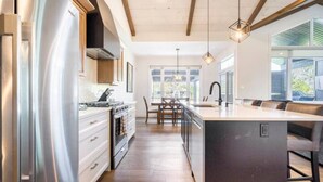A modern kitchen with a central island, stainless steel appliances, and a dining area with a chandelier. - Laporte Cottage | Hot Tub | Walk to Beach | Fire Pit | Grand Bend & Bayfield (Zurich)
