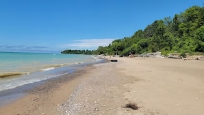 A beach with clear turquoise water, sandy shore, and dense green trees in the background. - Laporte Cottage | Hot Tub | Walk to Beach | Fire Pit | Grand Bend & Bayfield (Zurich)