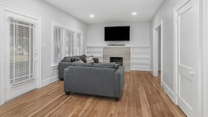 Ein modernes Wohnzimmer mit grauem Sofa, einem flachbildfernseher über einem Kamin und Holzboden.