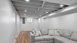 Ein modernes, minimalistisches Wohnzimmer mit einem grauen Ecksofa, gemusterten Kissen und Holzboden.