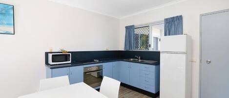 A compact kitchen with a microwave, stove, and refrigerator, a dining table with chairs, and a door with a blue curtain.