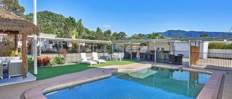 Una piscina al aire libre, sombrillas, sillones reclinables de piscina