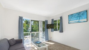 A modern living room with a grey sofa, a glass coffee table, and a painting of a beach scene. - Cocos Holiday Apartments (Trinity Beach)