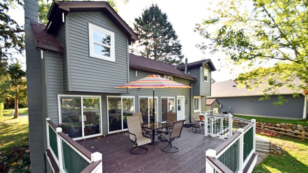 A deck with a table and chairs, a colorful umbrella, and a railing. - Kayaks - Firepit - Dock - Fishing & more! (Lindstrom)
