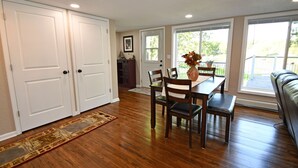 A dining area with a wooden table, chairs, and a vase of flowers. There are two white doors and a window with a view of the outdoors. - Kayaks - Firepit - Dock - Fishing & more! (Lindstrom)